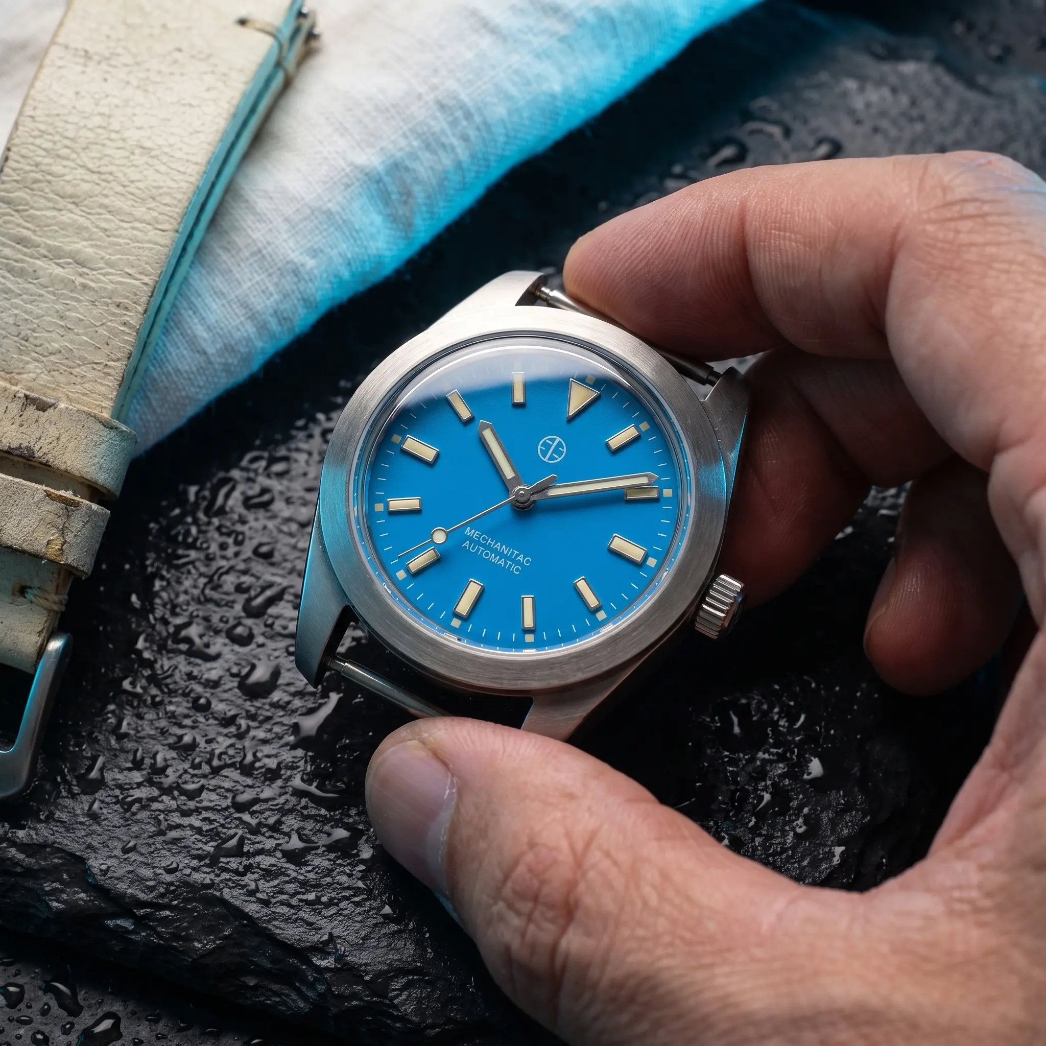 The steel dive watch on wet black slate with a soft azure rim light and fine water droplets around it