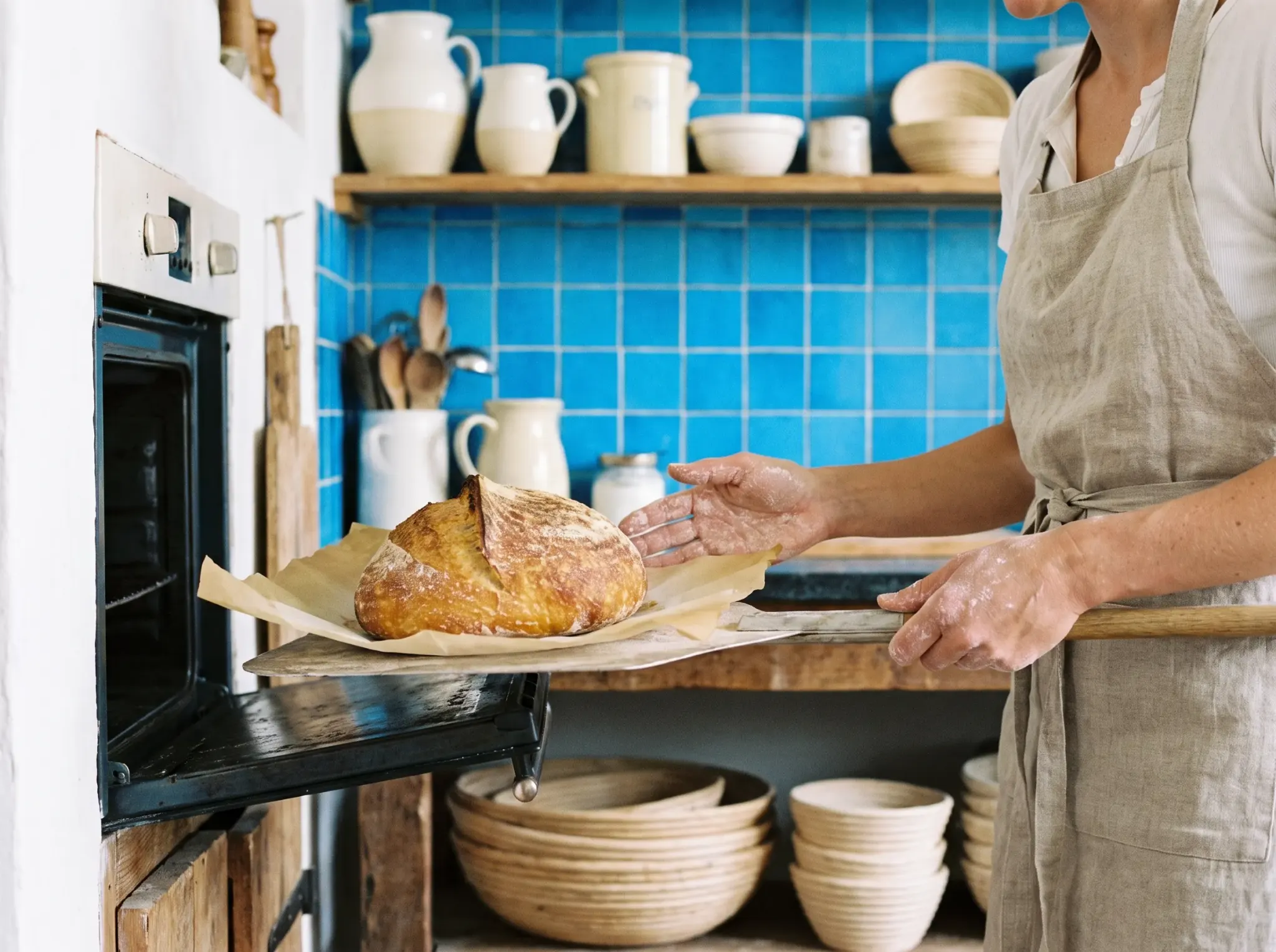 A home baker lifting a sourdough loaf from the oven