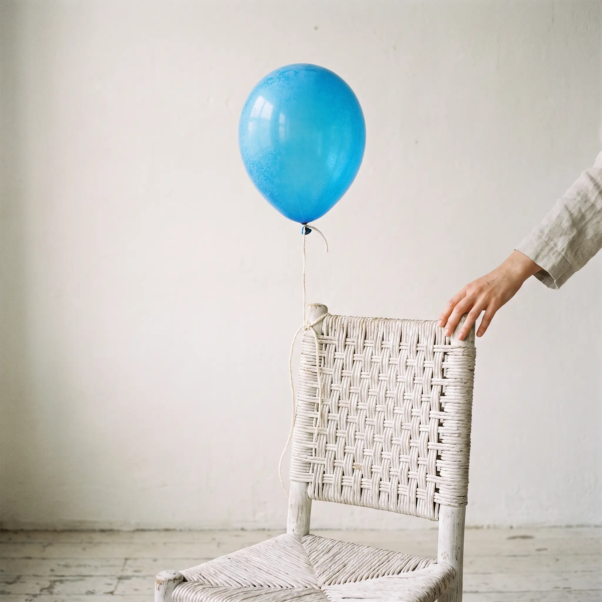 A single azure balloon tied to a white chair against a white wall