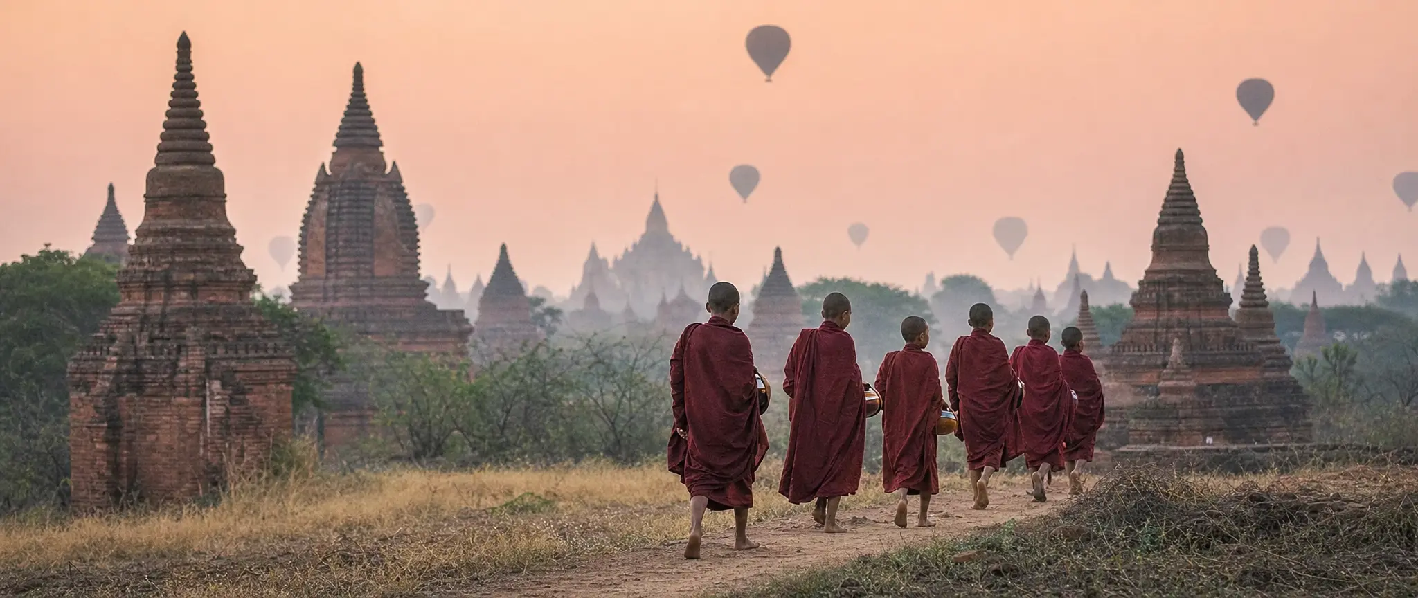 Young monks walking among ancient temples at dawn, balloons overhead