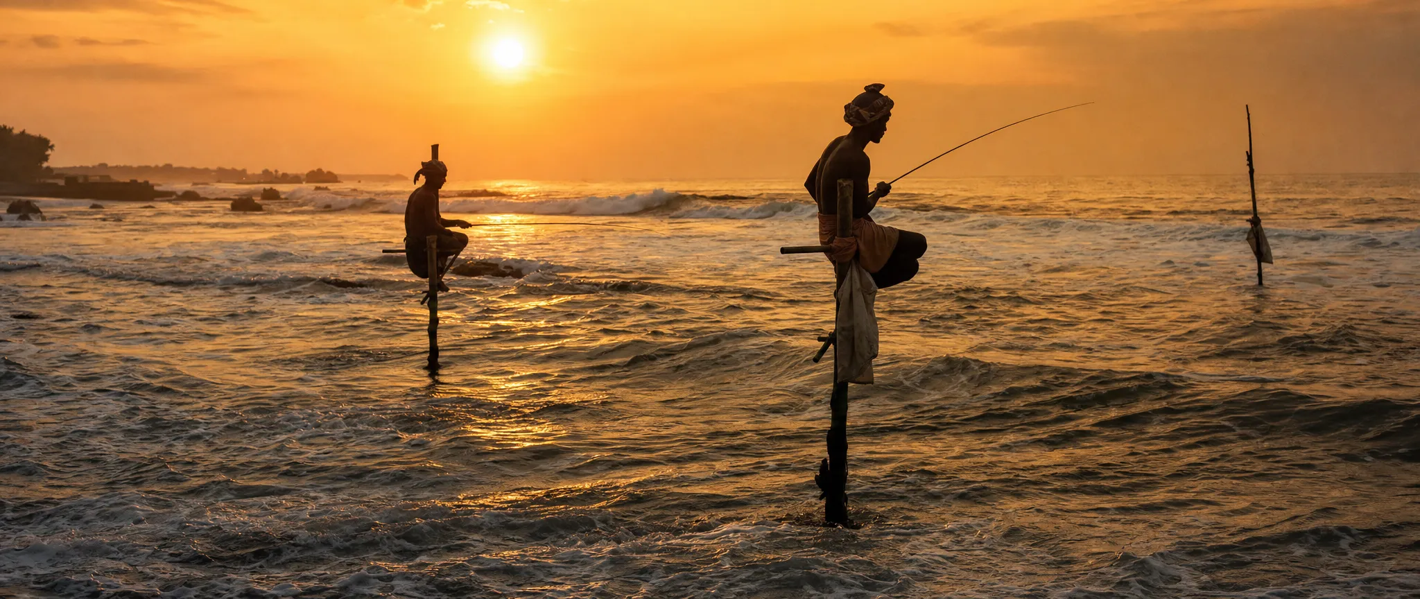 Stilt fishermen on poles in the surf at sunset