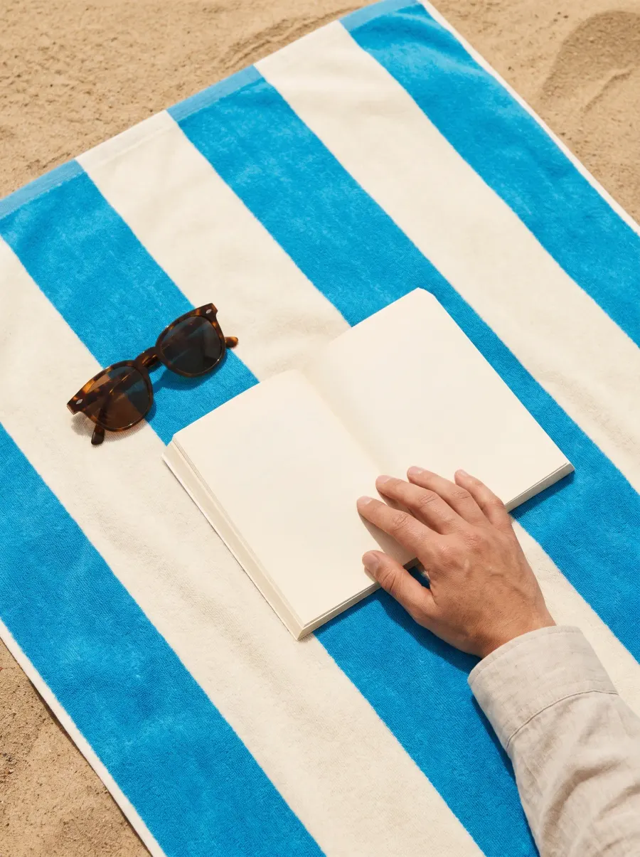 Sunglasses and a paperback on a striped azure beach towel