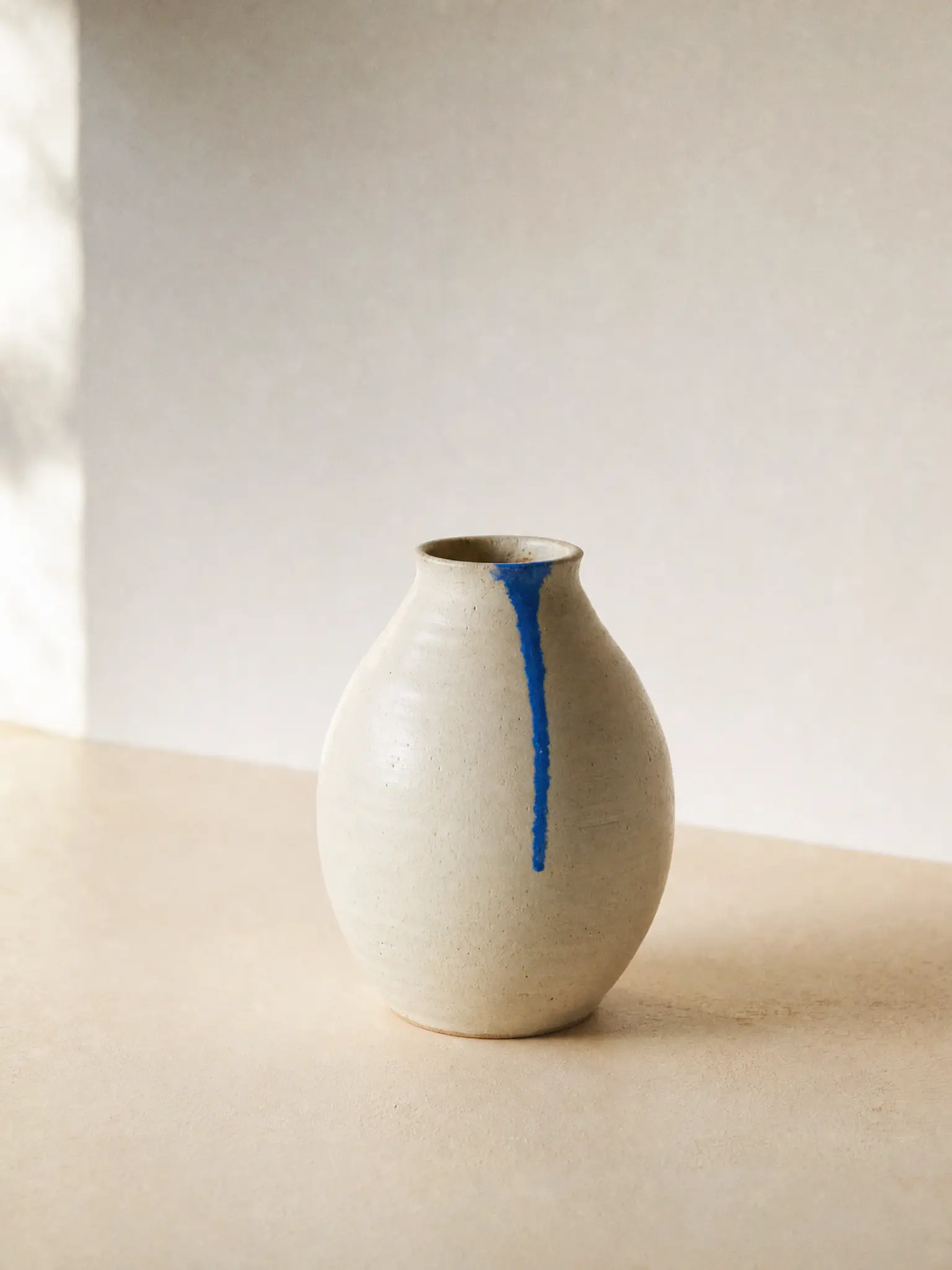 An ivory ceramic vase with an azure glaze drip