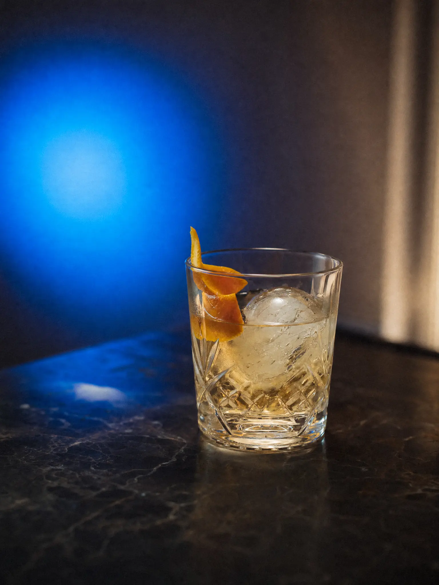 A cocktail with an ice sphere on black marble