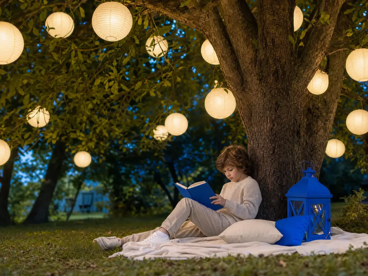 A child reading under a tree whose leaves are glowing paper lanterns