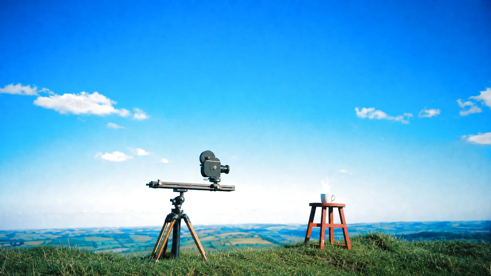 A cine camera on a slider on a hilltop, lined up on a steaming cup of coffee on a red stool
