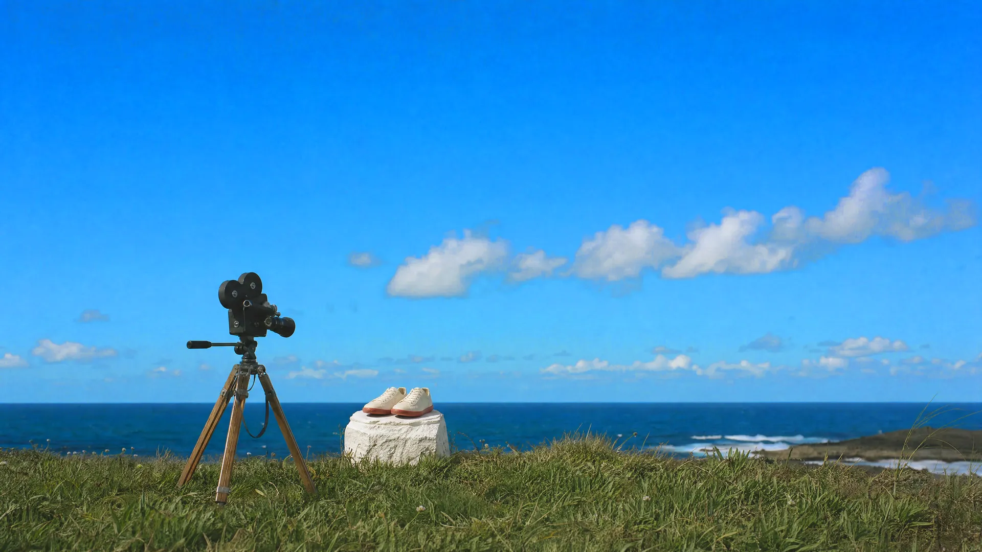 A vintage film camera on a tripod filming a pair of sneakers on a stone plinth by the sea