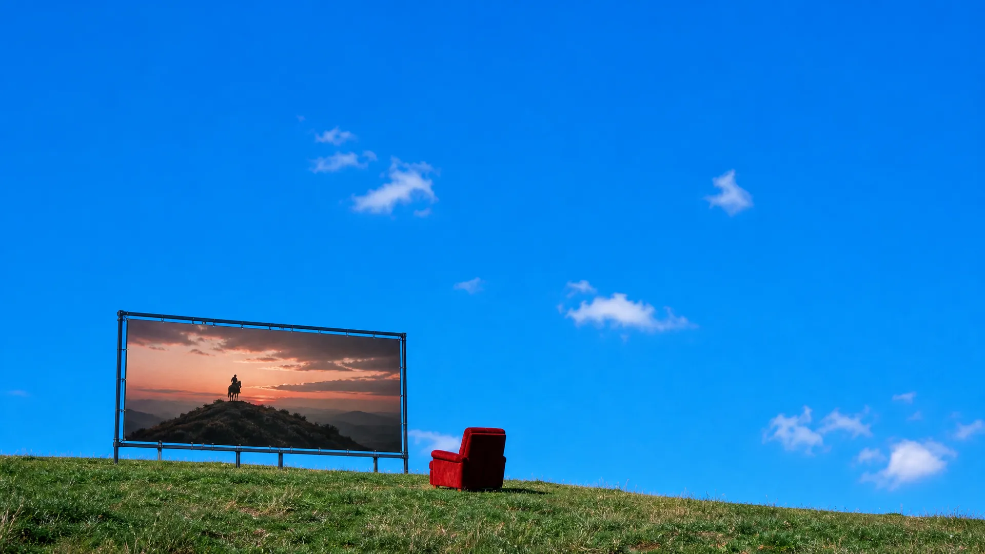 A wide movie screen on a hilltop showing a lone rider at dusk, a red velvet cinema seat facing it