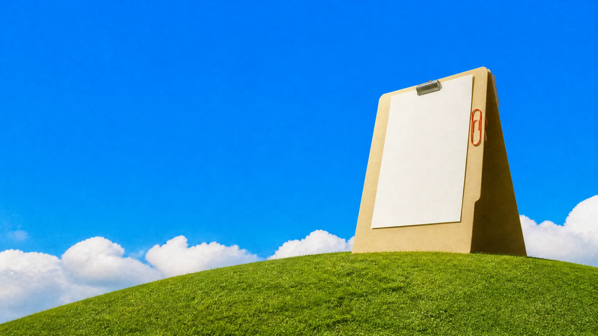 A giant manila folder standing open on a grassy hill with a blank sheet clipped inside and an orange paper clip.