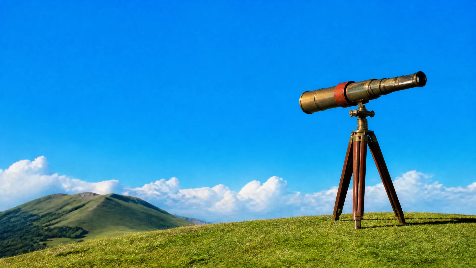 A brass telescope on a wooden tripod on a grassy hill, aimed at a neighbouring hill under a blue sky.