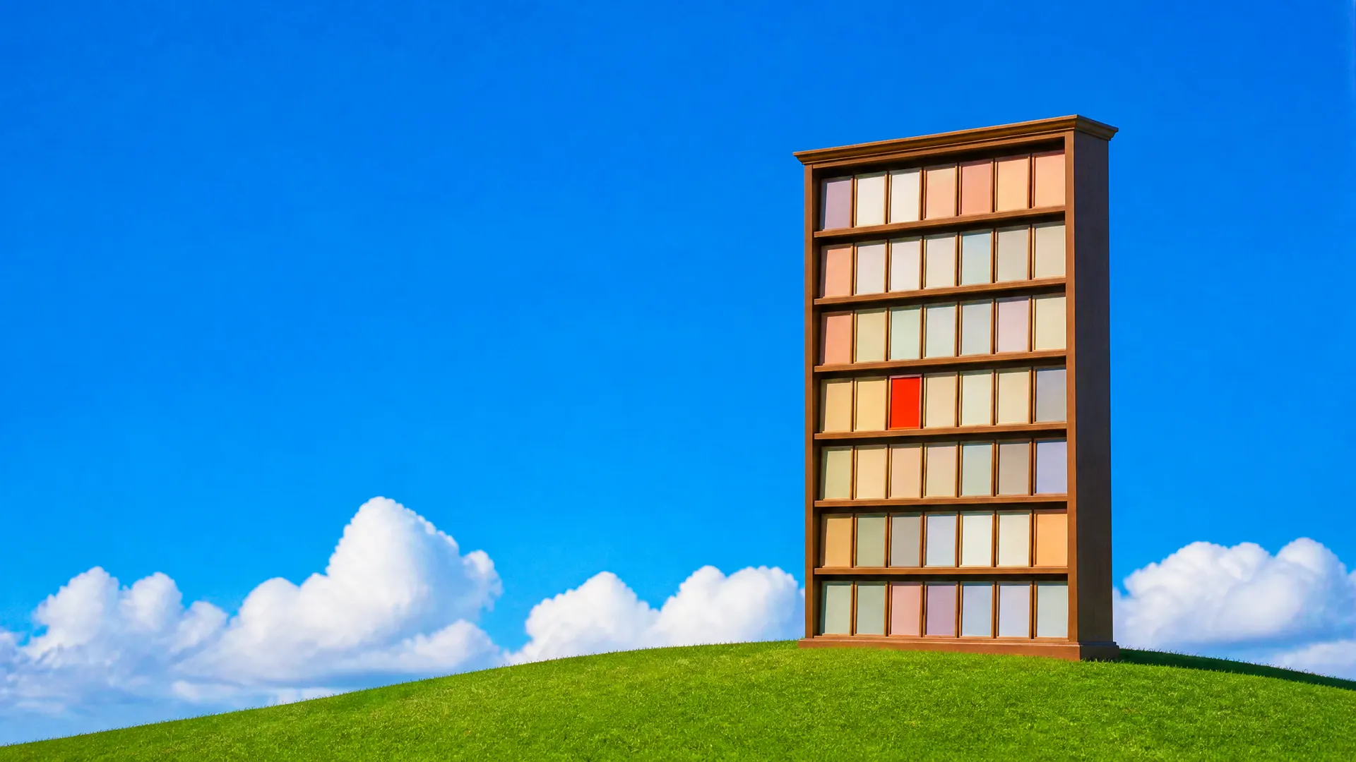 A tall wooden bookcase filled with blank pastel poster boards, one orange, standing on a grassy hill.