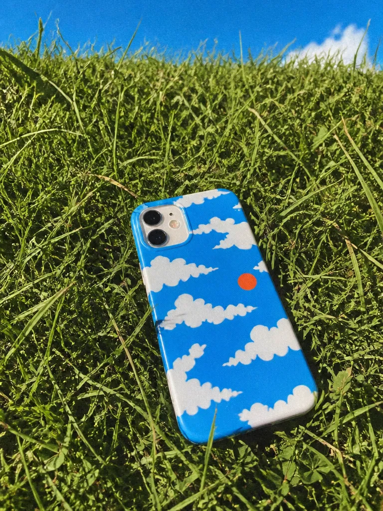 A phone in a printed cloud case on grass