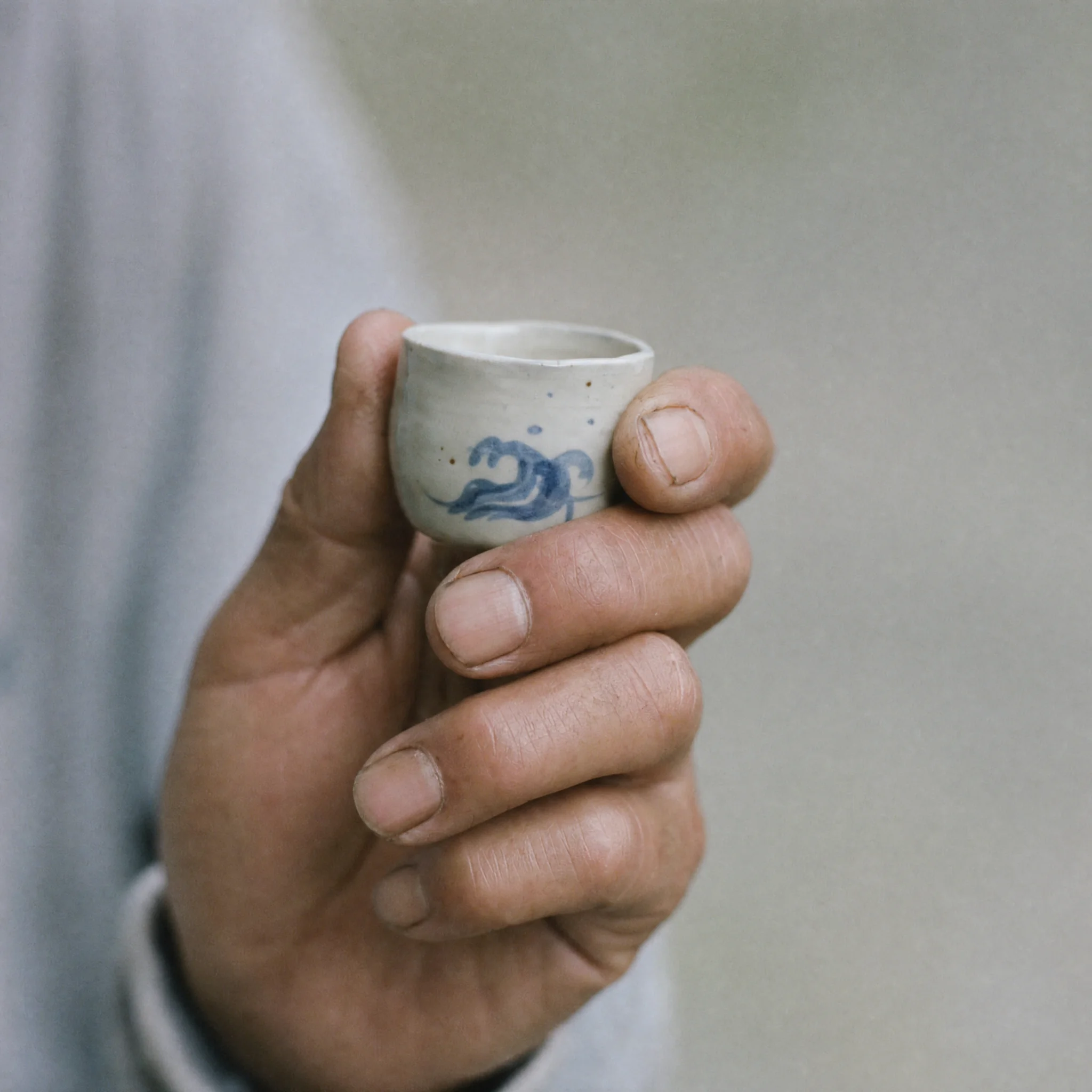 A hand holding a ceramic cup with a tiny painted wave