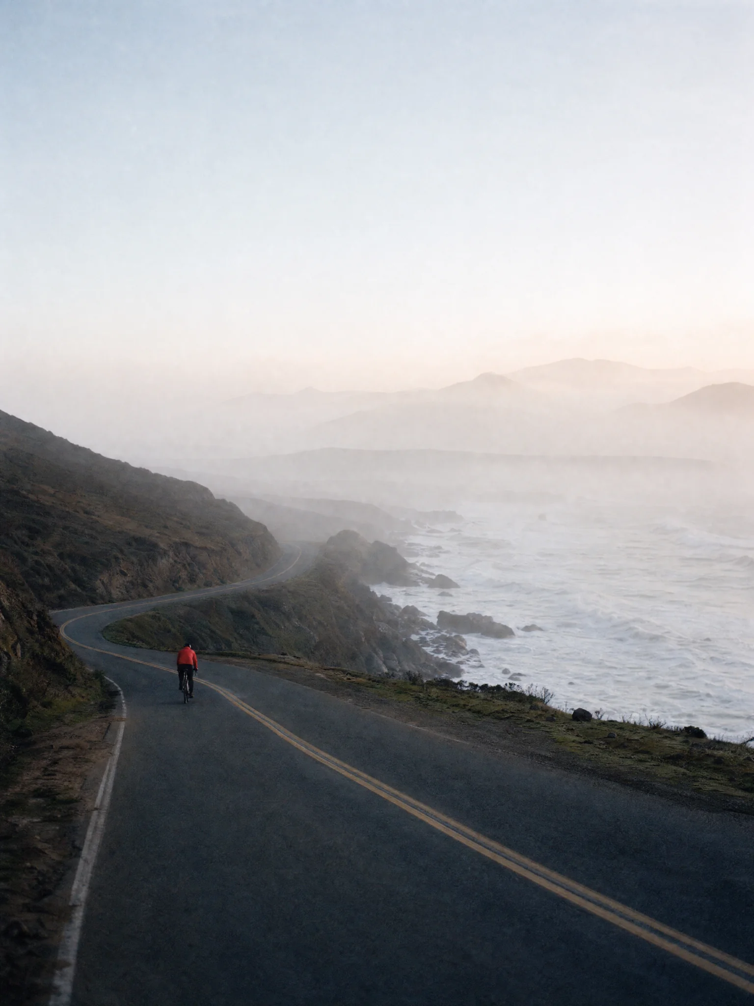 A cyclist in a vermilion jacket on an empty coast road