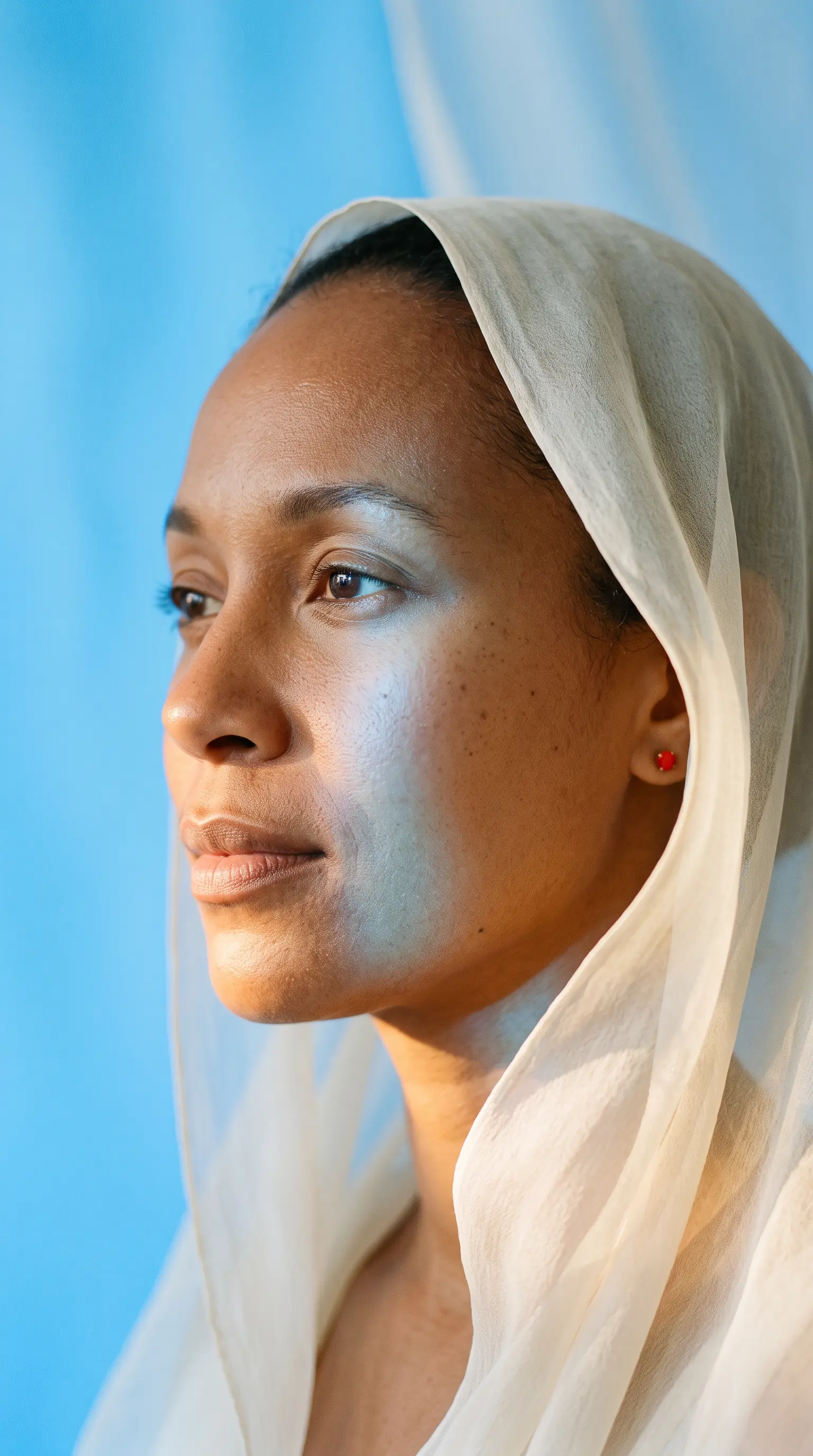 An editorial portrait of a woman in an ivory veil with blue reflected light