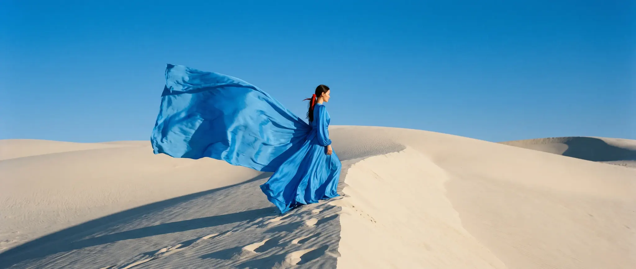 A model in a billowing azure silk gown on an ivory dune crest