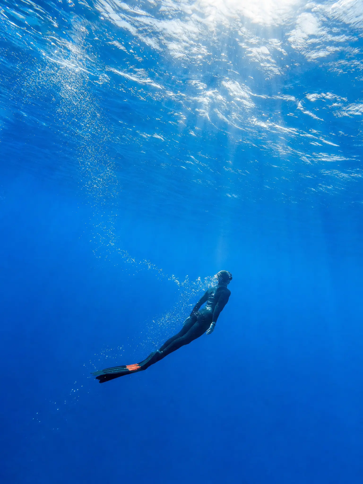 A freediver beneath the luminous surface of a deep blue sea