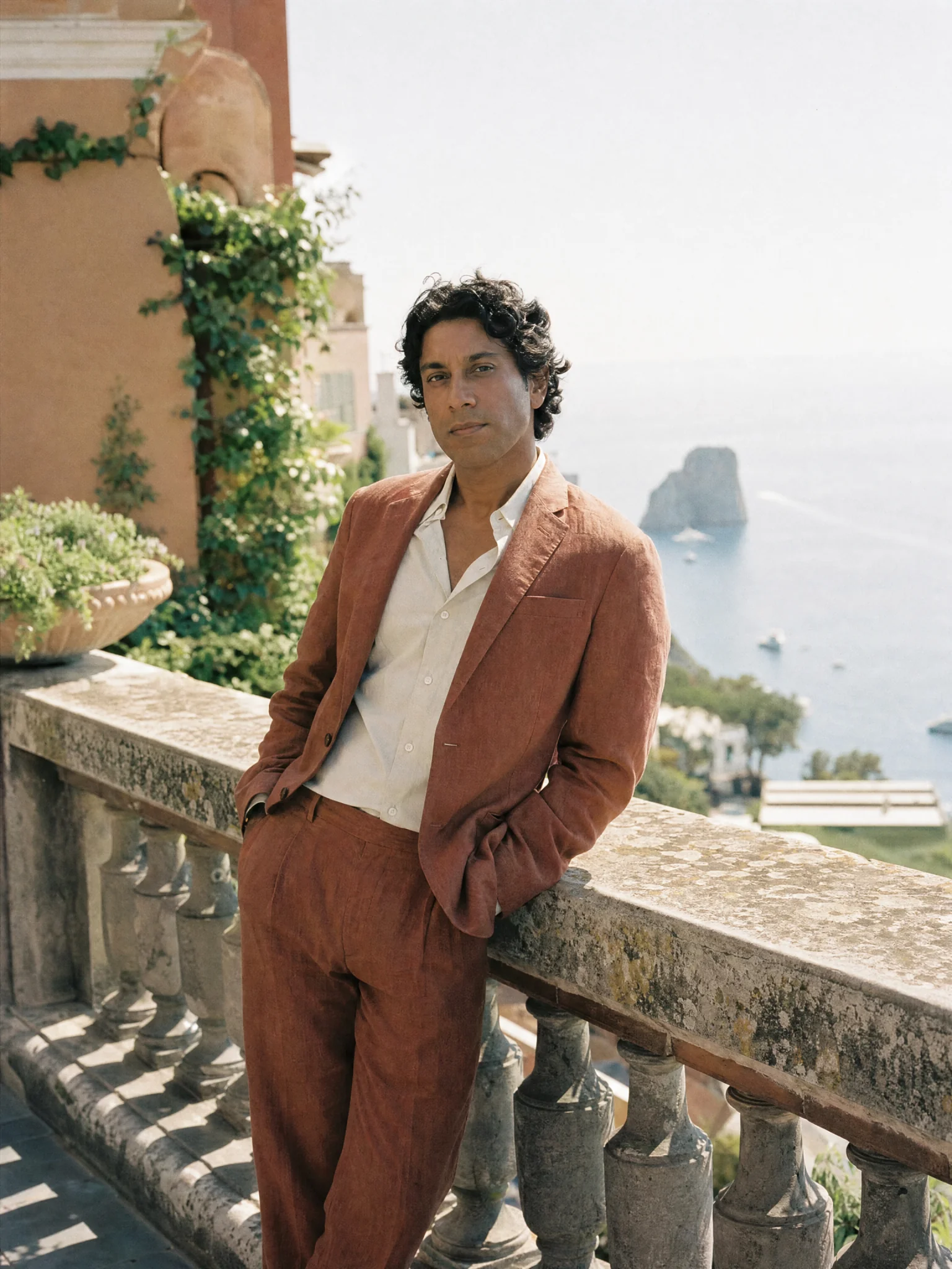 A man in a rust linen suit on a sunlit terrace