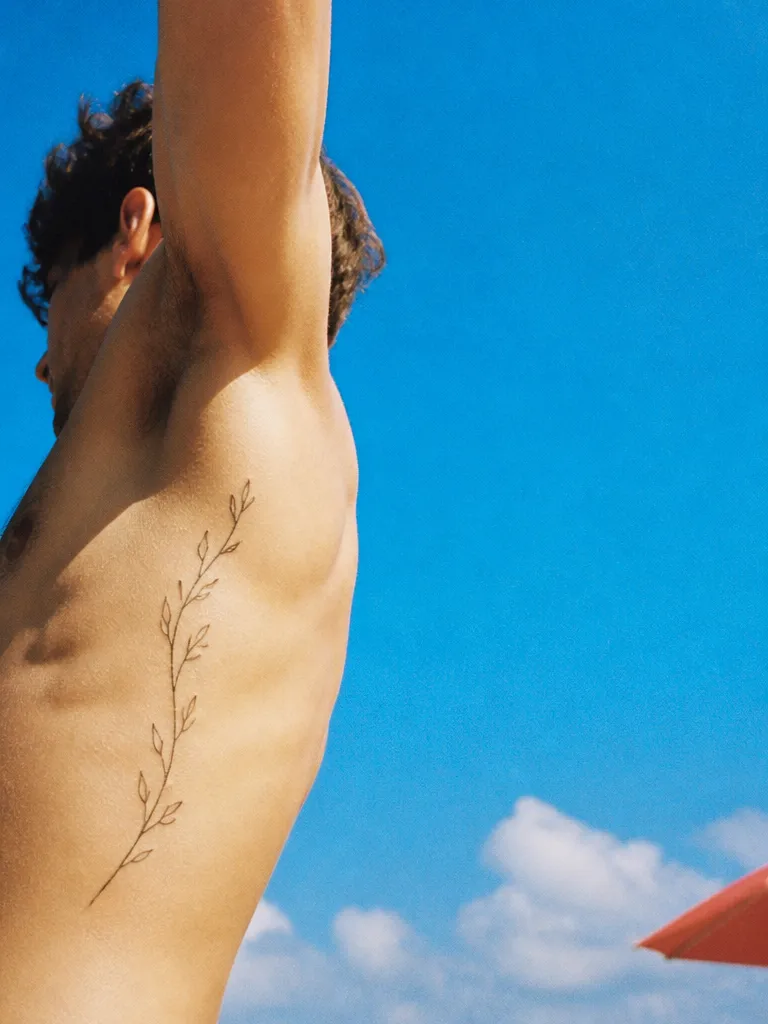 A fine-line branch tattoo along the ribs