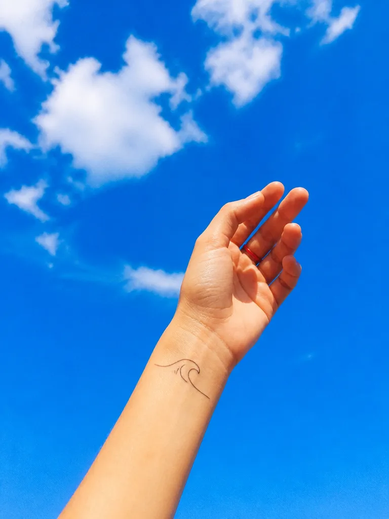A single-line wave tattoo on a wrist